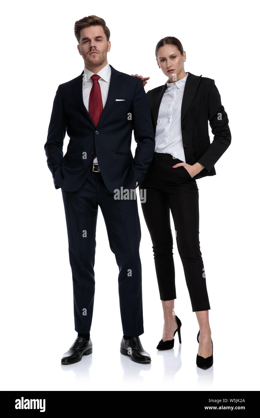 couple in business suits looking serious with hands on pockets and shoulder on white background Stock Photo