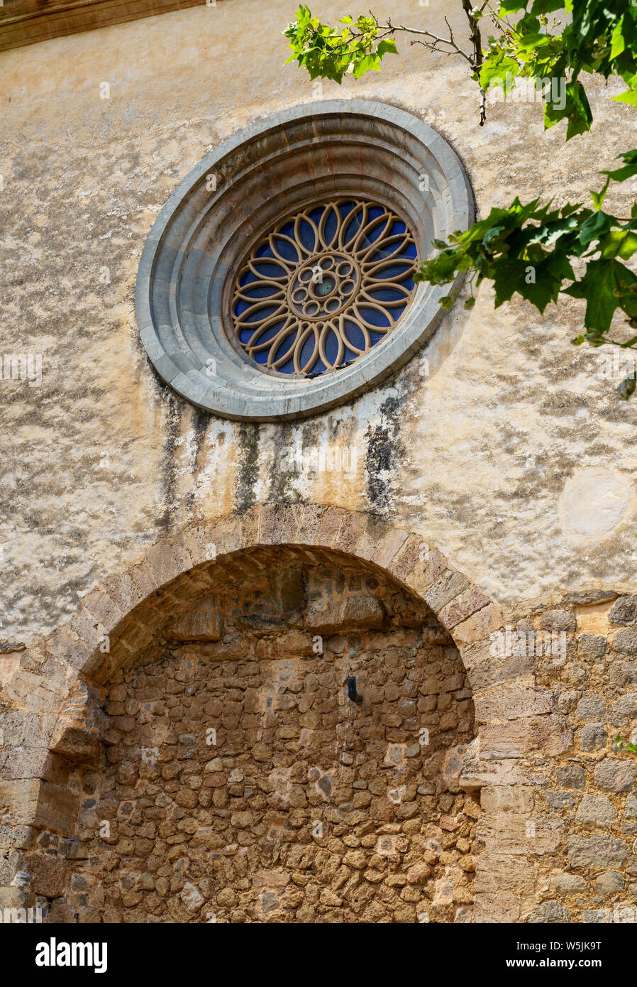 Detail shot of the royal charter house of Jesus of nazareth in Valldemossa - rough brick wall with a beautiful round window behind green leaves Stock Photo