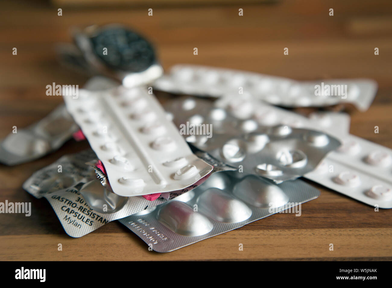 Tabletop photograph of several strips of prescription drugs with a wristwatch in the background to indicate time-sensitive dosing. Stock Photo