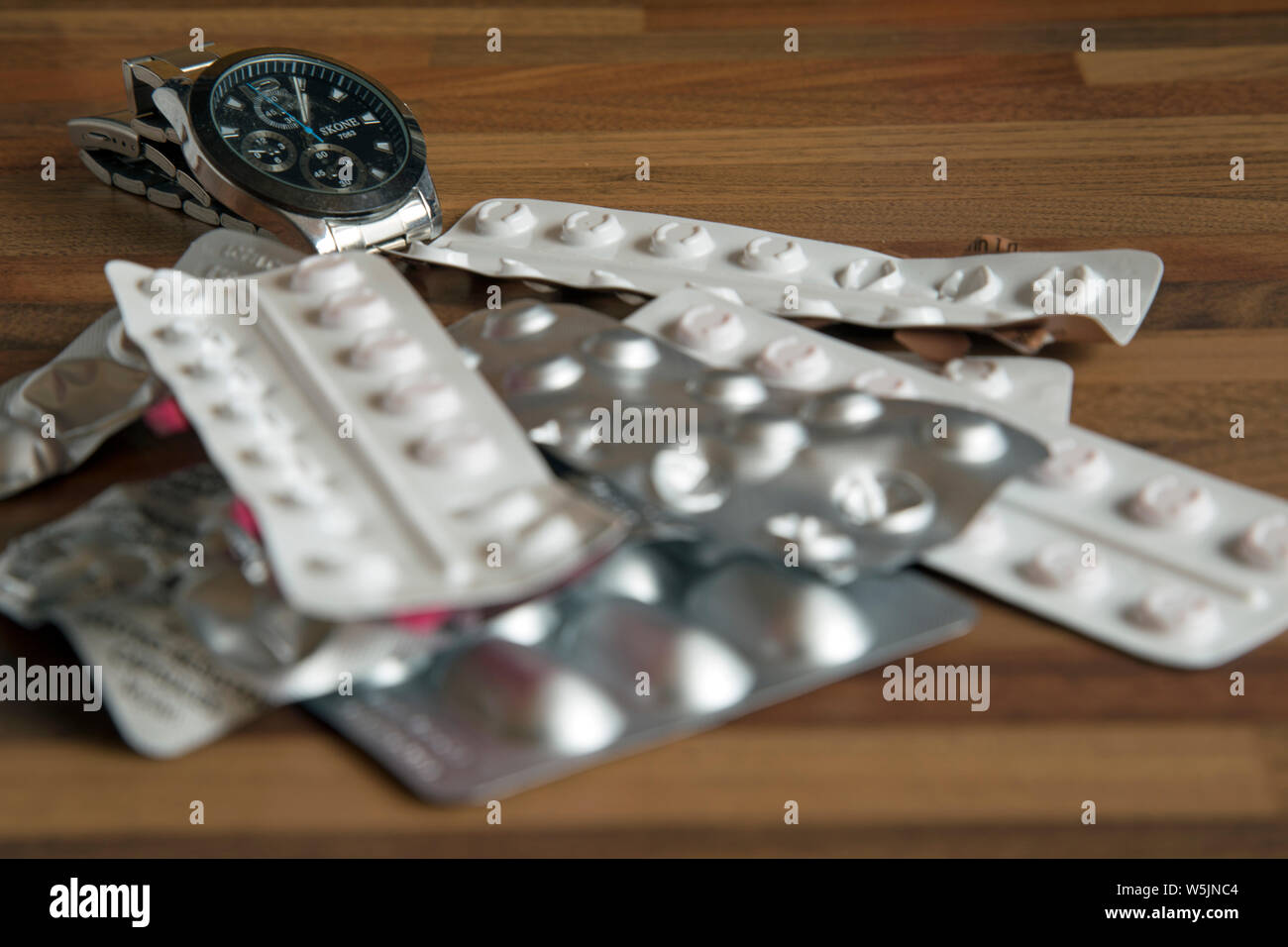 Tabletop photograph of several strips of prescription drugs with a wristwatch in the background to indicate time-sensitive dosing. Stock Photo