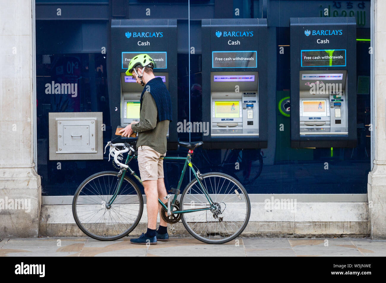 A man on a racing bicycle with cycle helmet gets cash from a Barclays Bank cash machine or ATM Stock Photo