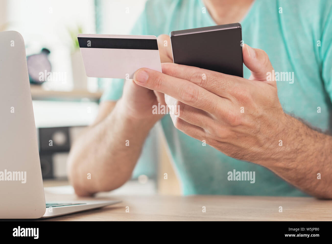 Online shopping with credit card and smart phone, casual man is using smartphone app in home office to purchase items on internet Stock Photo