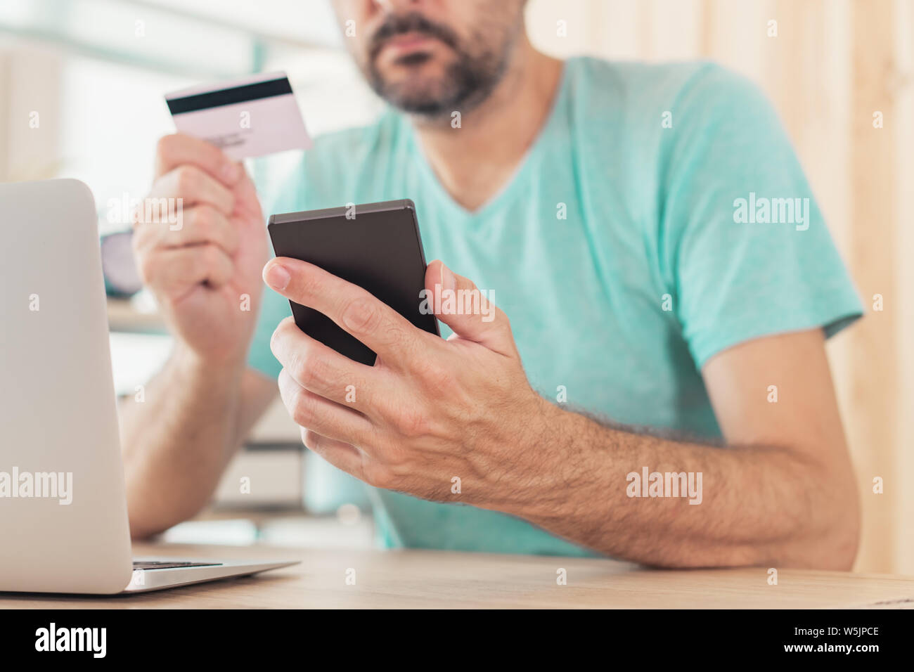 Online shopping with credit card and smart phone, casual man is using smartphone app in home office to purchase items on internet Stock Photo