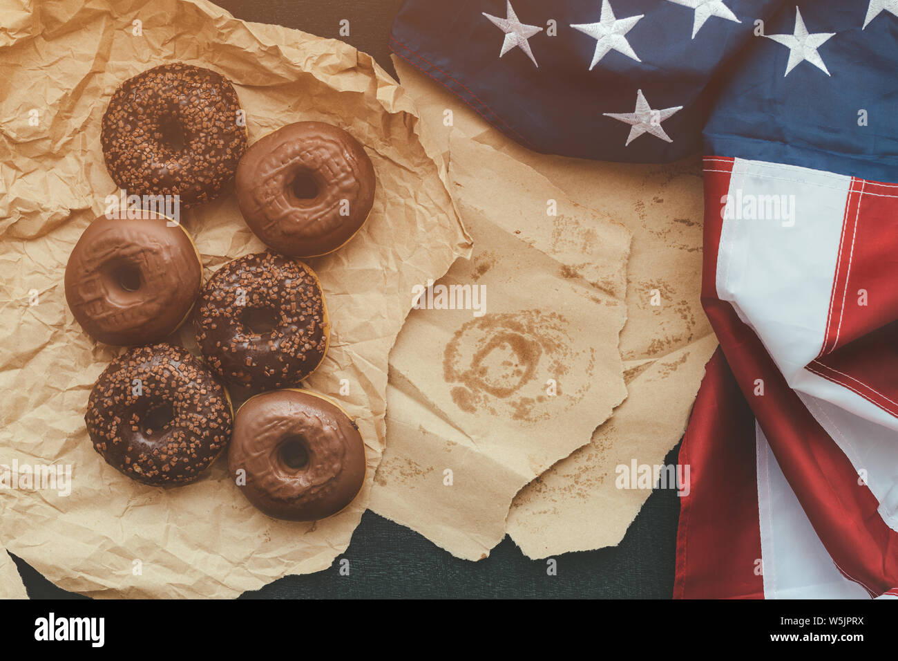 Sweet chocolate donuts and american flag, top view on the table. Traditional homemade doughnut pastry with cream and chocolate crumbs. Stock Photo