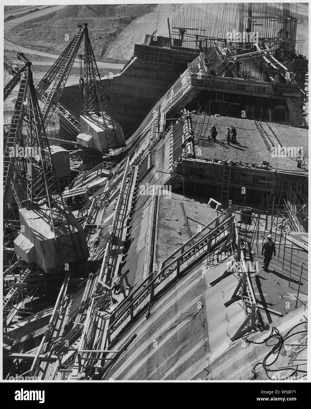 A view of the partially completed ogee section of the spillway. Material for this structure was handled by stiff-leg derricks shown in the left of the picture.   Project Los Angeles River Improvement. Location Hansen Dam across Tujunga Wash. Funds Regular funds. Work prosecuted under Contract No. W-509-Eng.689. Stock Photo