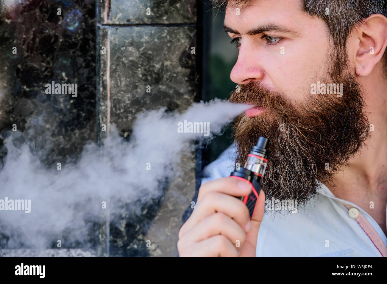 Man with beard breathe out smoke. Smoking electronic cigarette. Stress  relief concept. Smoking device. Man long beard relaxed with smoking habit.  Clouds of flavored smoke. Bearded man smoking vape Stock Photo -