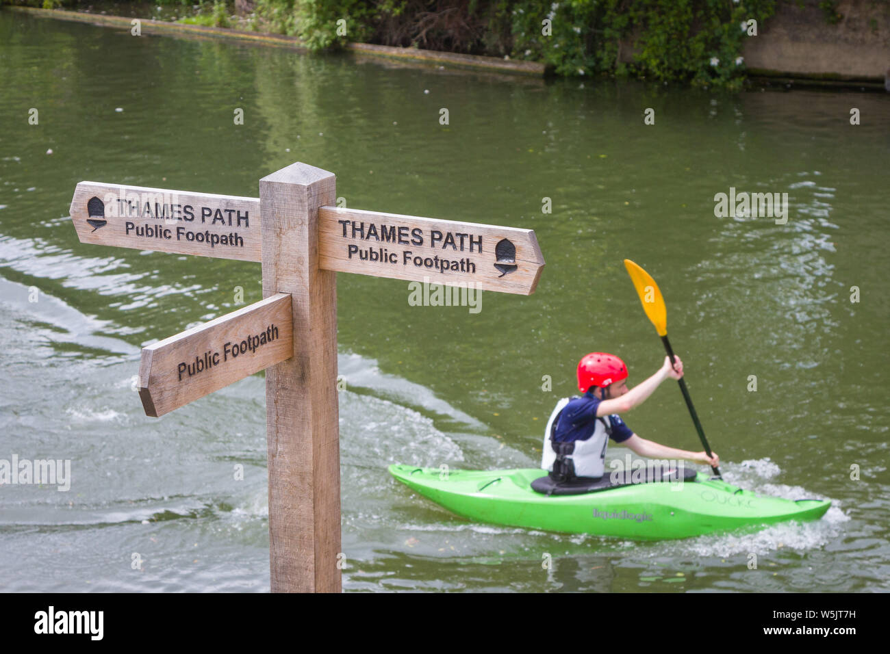 A man in a canoe passes a wooden sign for the Thames Path Public Footpath on hte Thames at Oxford Stock Photo