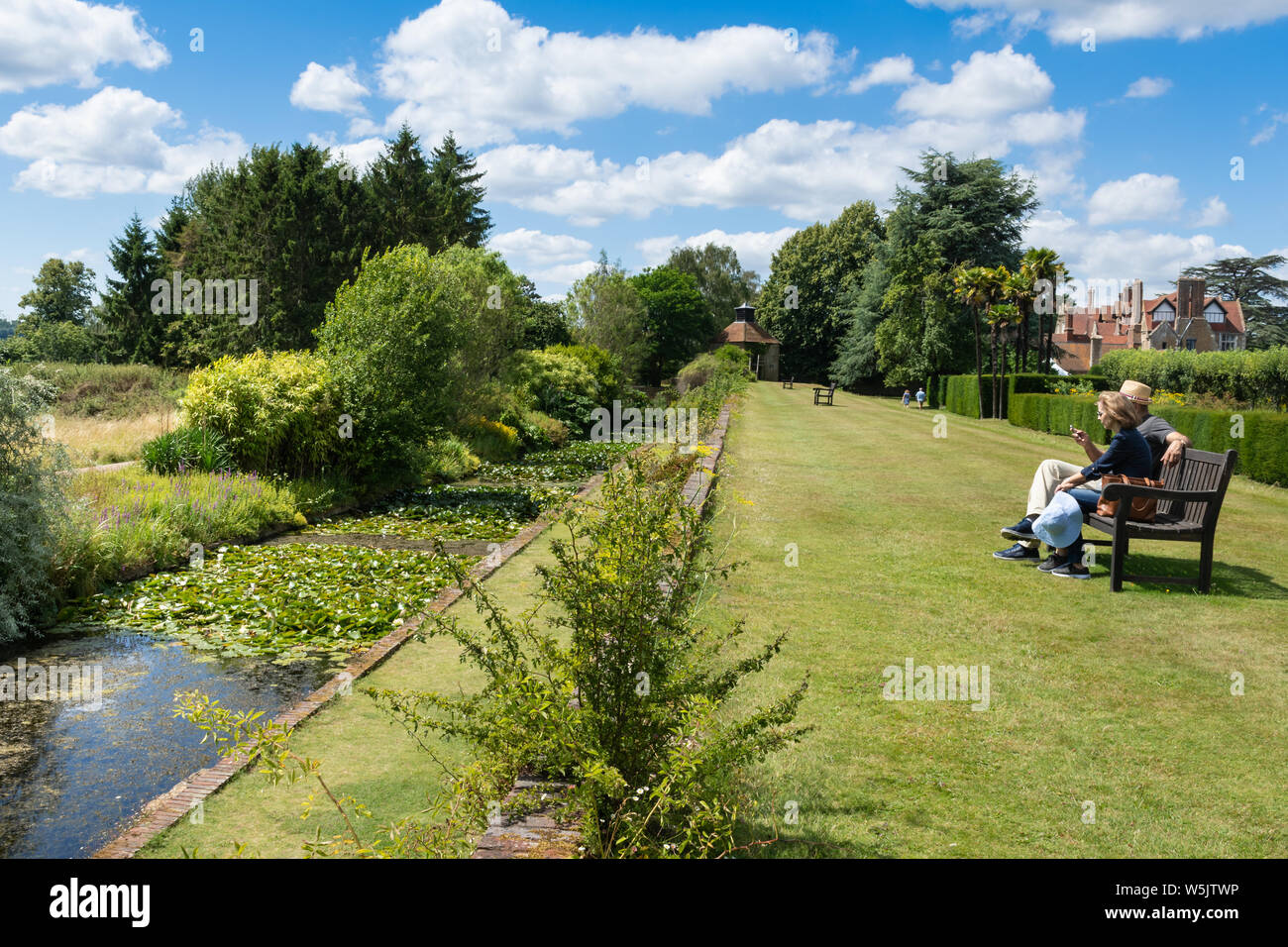 Visitors overlooking the moat and enjoying the gardens at Loseley Park, Surrey, UK, during summer Stock Photo