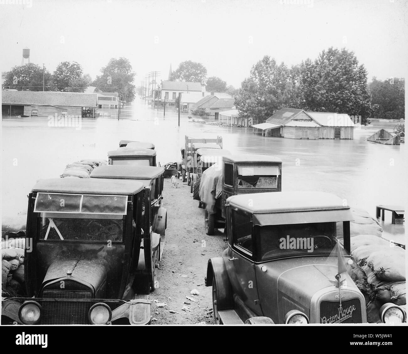 Aerial photograph of flood, unidentified stretch of lower Mississippi River.; Scope and content:  Flooded neighborhood. Cars and trucks in foreground where the streets emerges from the floodwater; inundated buildings along the flooded town street in background. Stock Photo