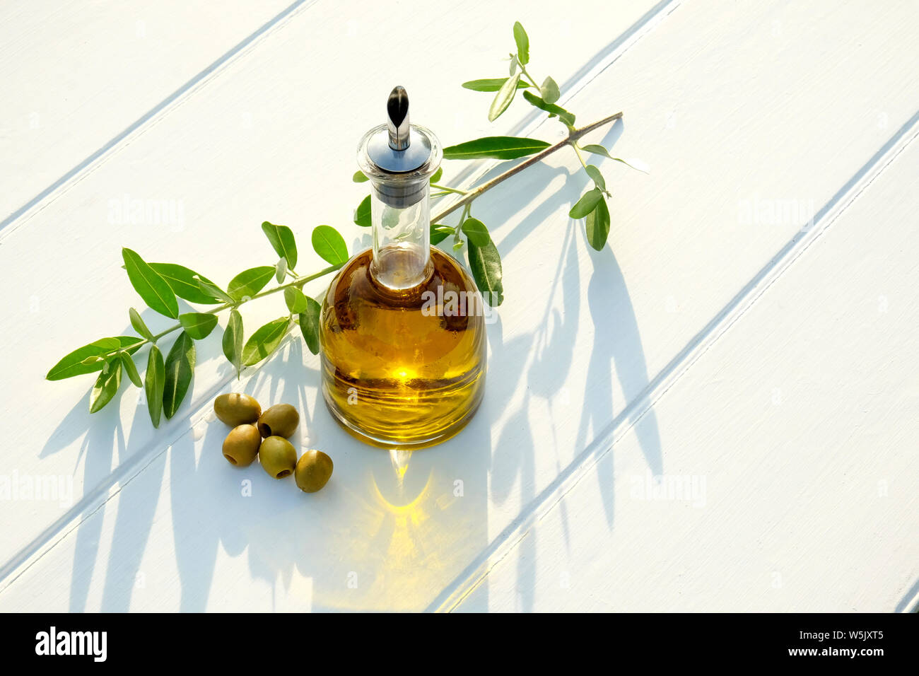 https://c8.alamy.com/comp/W5JXT5/olive-oil-in-a-glass-pouring-bottle-scattered-around-the-bottom-of-the-bottle-are-five-individual-olives-behind-the-jar-is-an-olive-branch-with-gree-W5JXT5.jpg