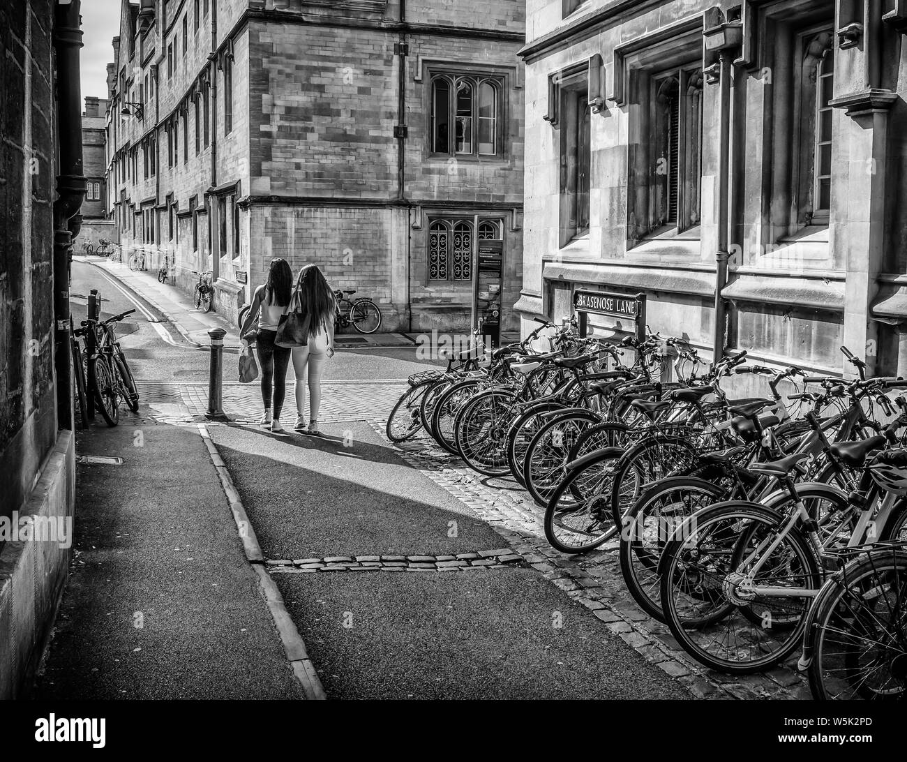 Row of bicycles by Brasenose College, Oxford, with two young women passing (monochrome) Stock Photo