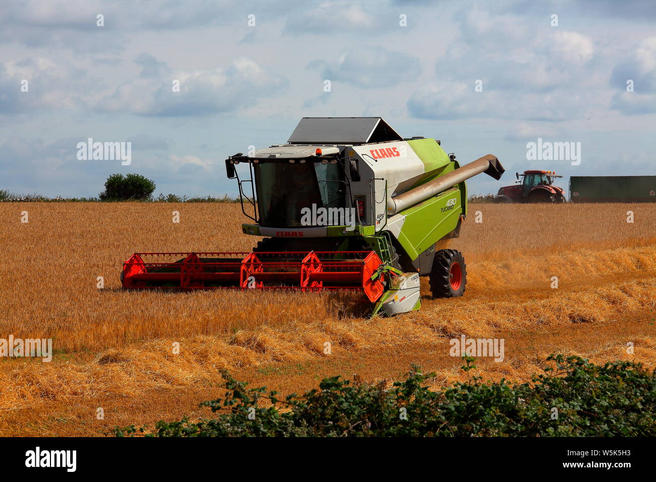 A combine harvester works it way around a small field in the countryside gathering this years crop of wheat making short work of this years crop. Stock Photo