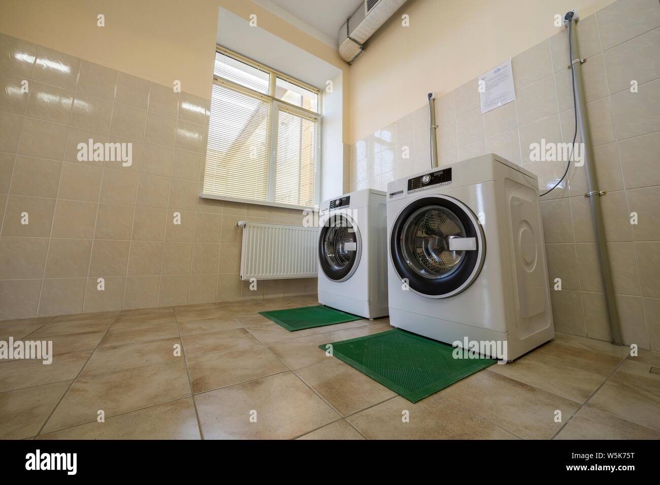Modern new industrial washing machines on rubber insulation mats in clean  light tiled bathroom or laundry room with air ventilation system Stock  Photo - Alamy