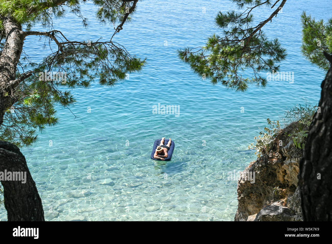 Unrecognizable tourist enjoys the beach at Brela. The Makarska riviera in Croatia is famous for its beautiful pebbly beaches and crystal clear water. Stock Photo