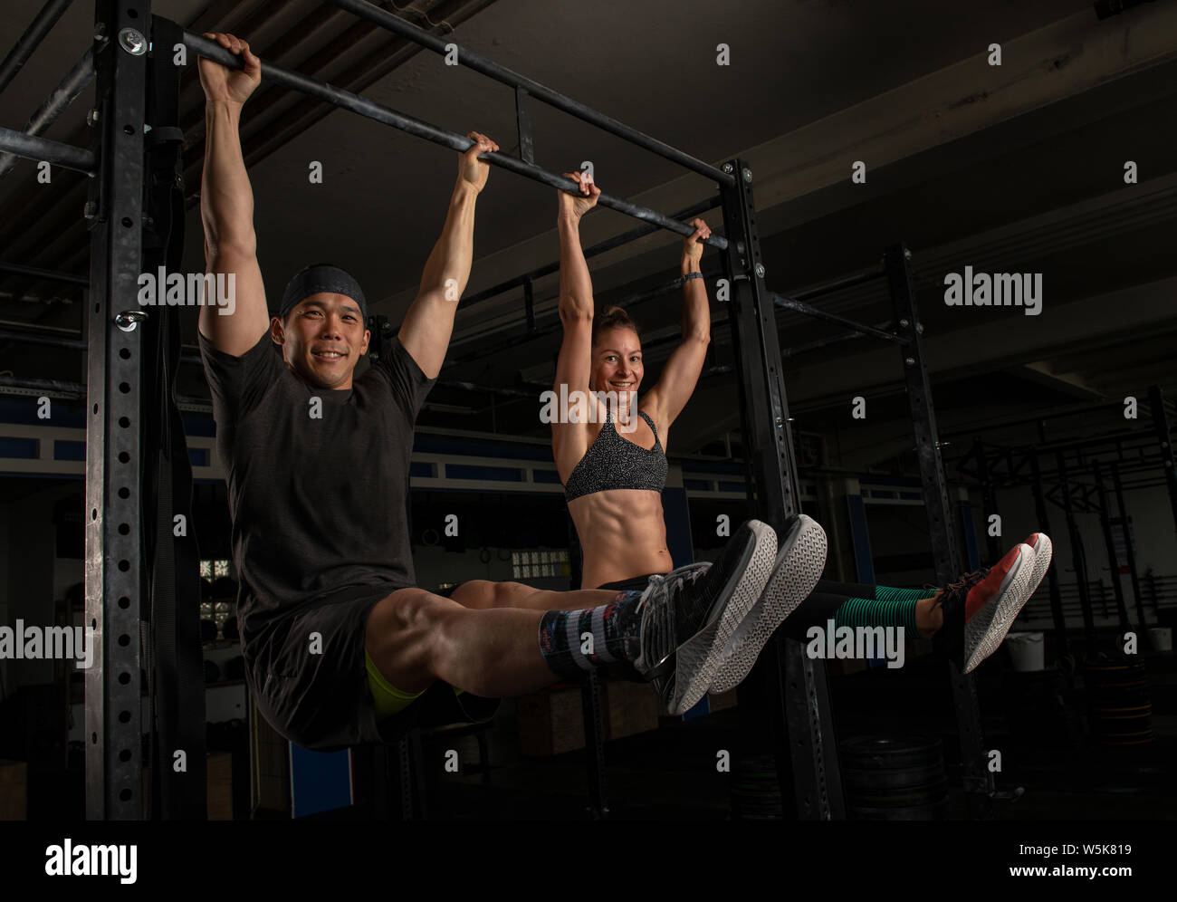 A fit couple is doing a functionalists fitness training together and having fun.The sporty and beautiful man and woman are doing the exercise l sit Stock Photo
