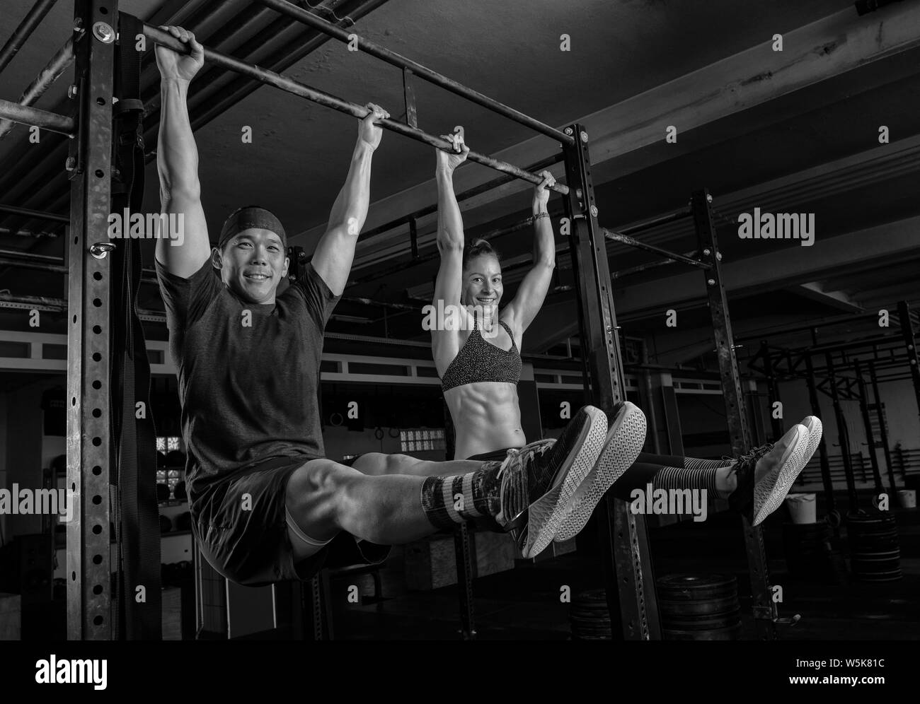 An athletic couple is doing a fitness workout together and having fun.The muscular and attractive man and woman are doing the exercise l sit. Stock Photo