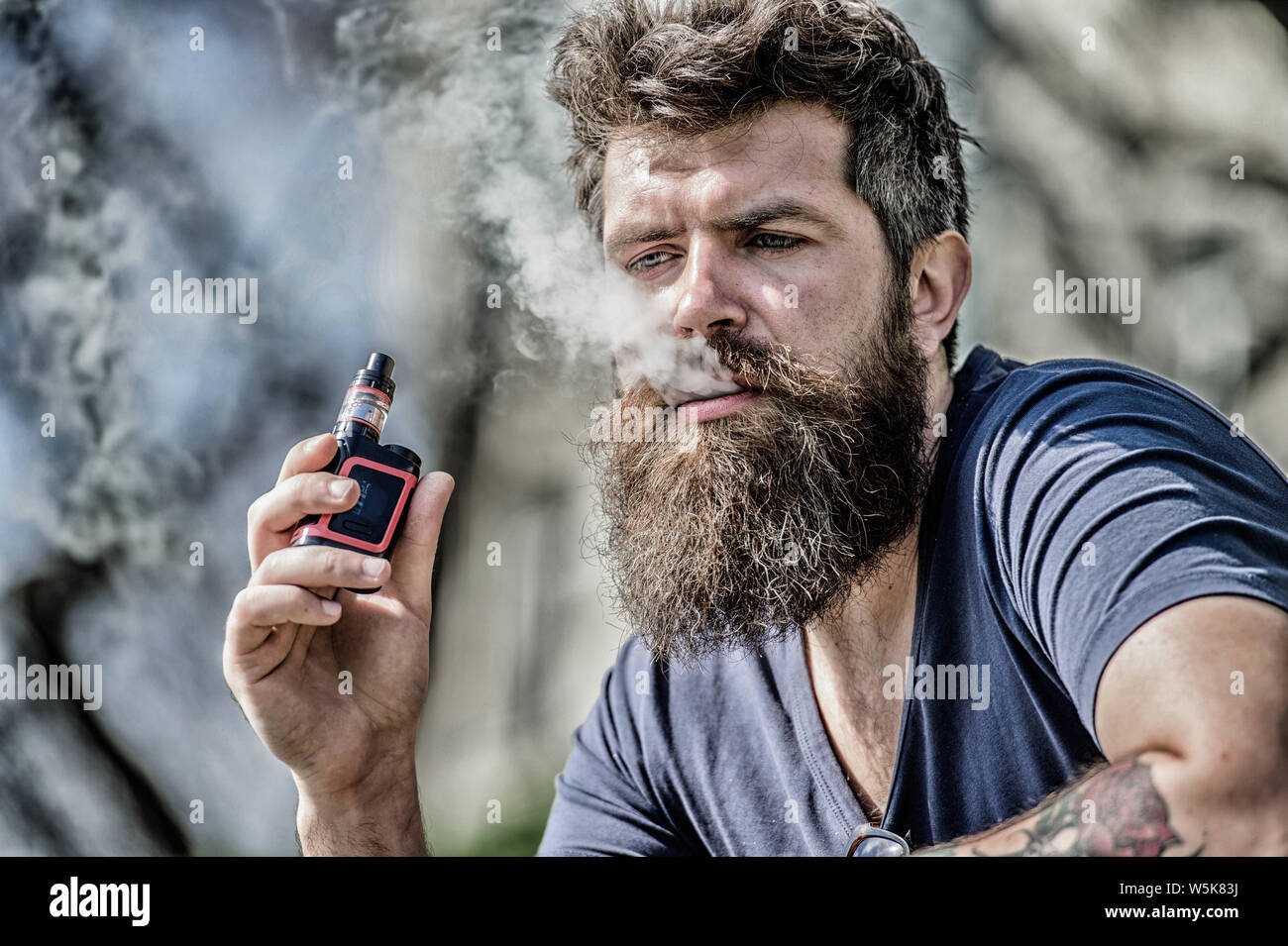 Man with beard breathe out smoke. Clouds of flavored smoke. Bearded man smoking  vape. Smoking electronic cigarette. Stress relief concept. Smoking device.  Man long beard relaxed with smoking habit Stock Photo -