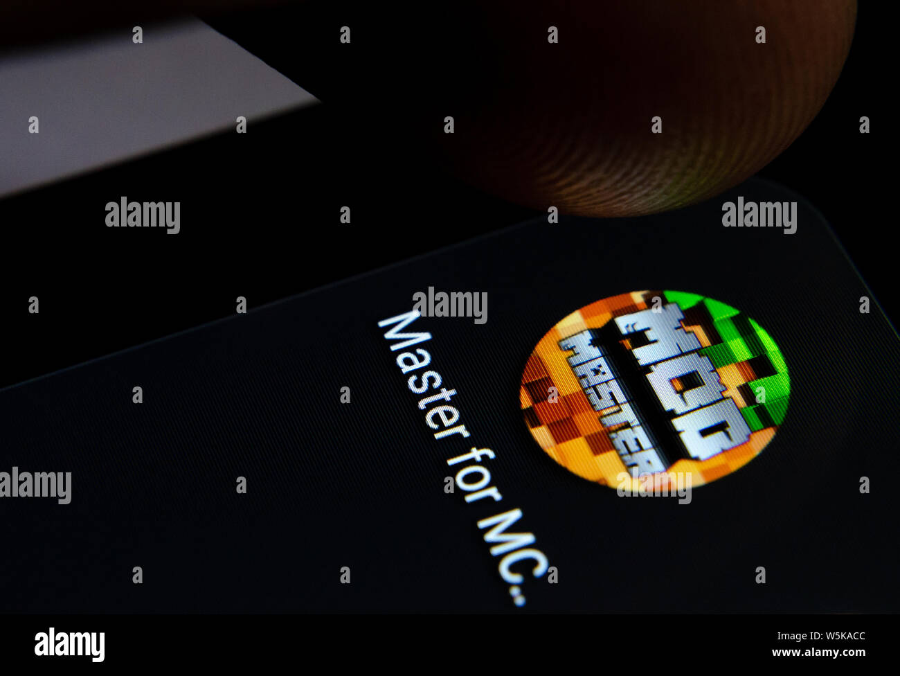 Minecraft Master MOD app icon on the smartphone screen with visible pixels and the finger about to launch it. Stock Photo