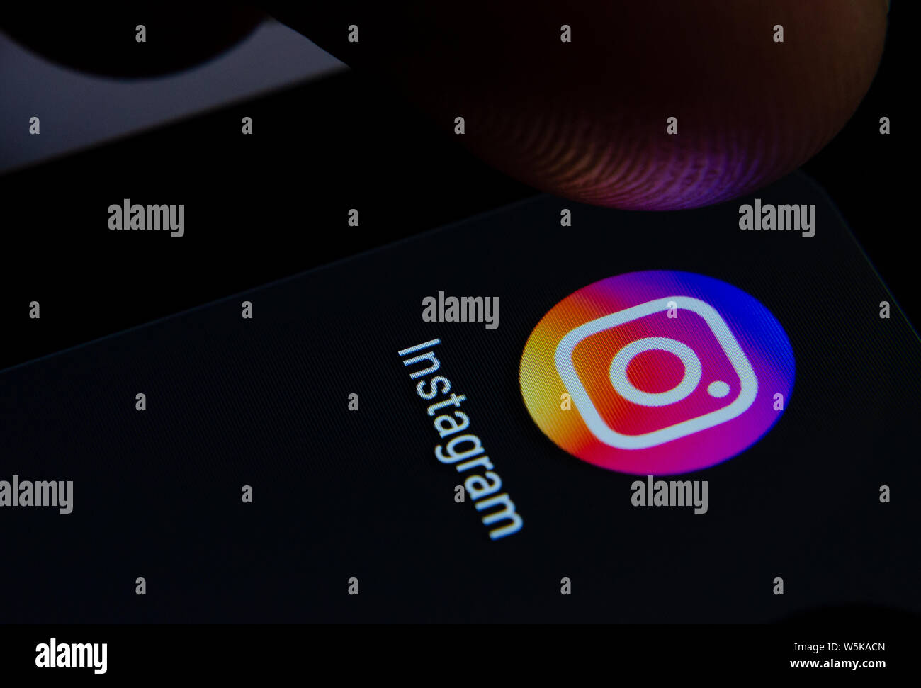 Instagram app icon on the smartphone screen with visible pixels and the finger about to launch it. Stock Photo