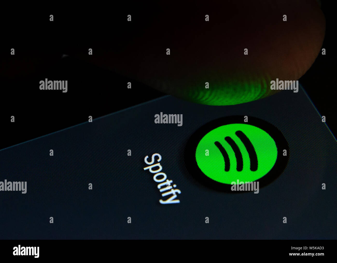 Spotify app icon on the smartphone screen with visible pixels and the finger about to launch it. Stock Photo