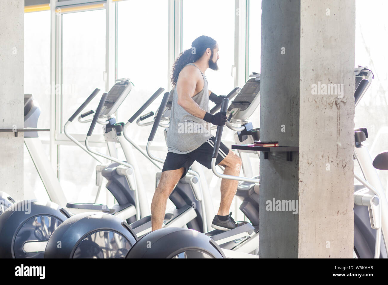 Side view of young adult sport man with long curly hair training at gym