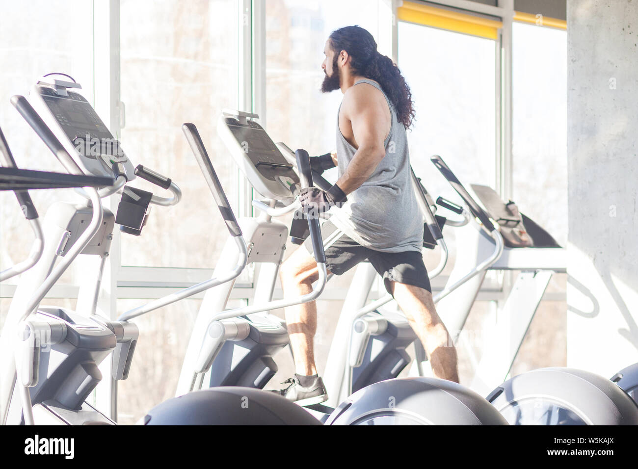 Side view of young adult sport man with long curly hair training at gym