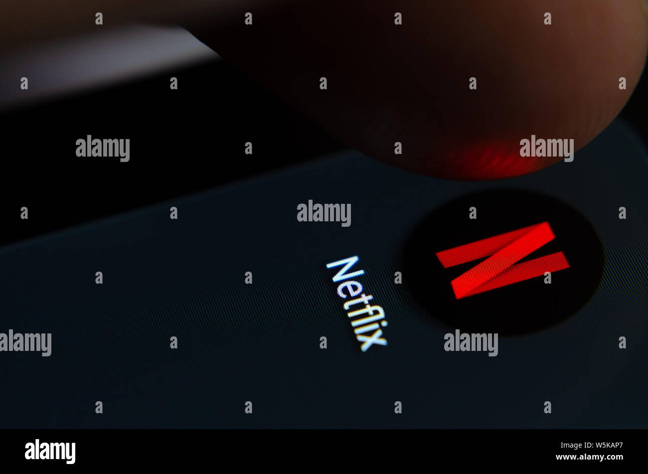 Netflix app icon on the smartphone screen with visible pixels and the finger about to launch it. Stock Photo
