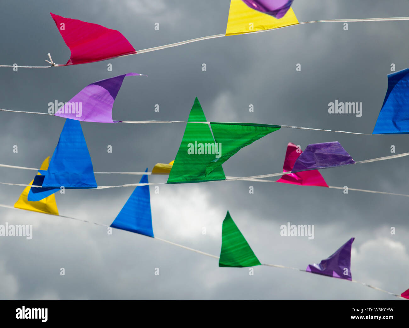 Several strings of brightly coloured pennant bunting set against a stormy dark sky Stock Photo