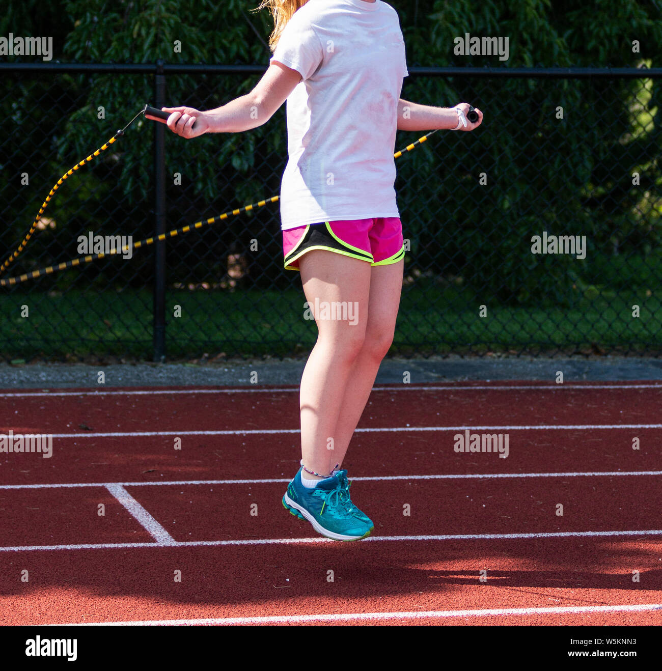 A high school runner is cross training using a black and white jump rope in the shade on the track during a warm practice. Stock Photo