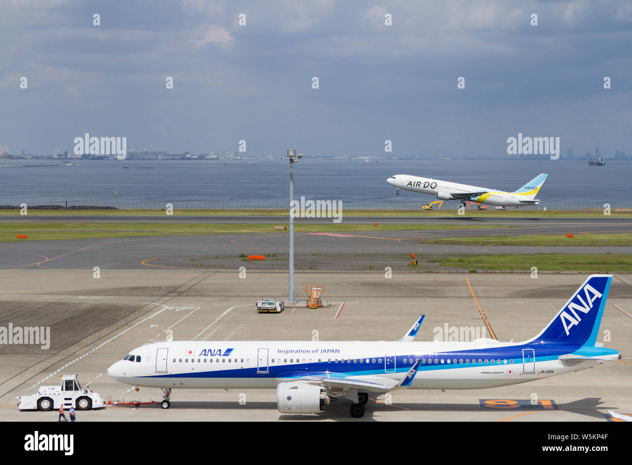 An All Nippon Airways Ana Airbus A321 272n On The Apron While An Air Do Boeing 767 381 Er Takes Off From The Runway Behind At Haneda Airport Toky Stock Photo Alamy