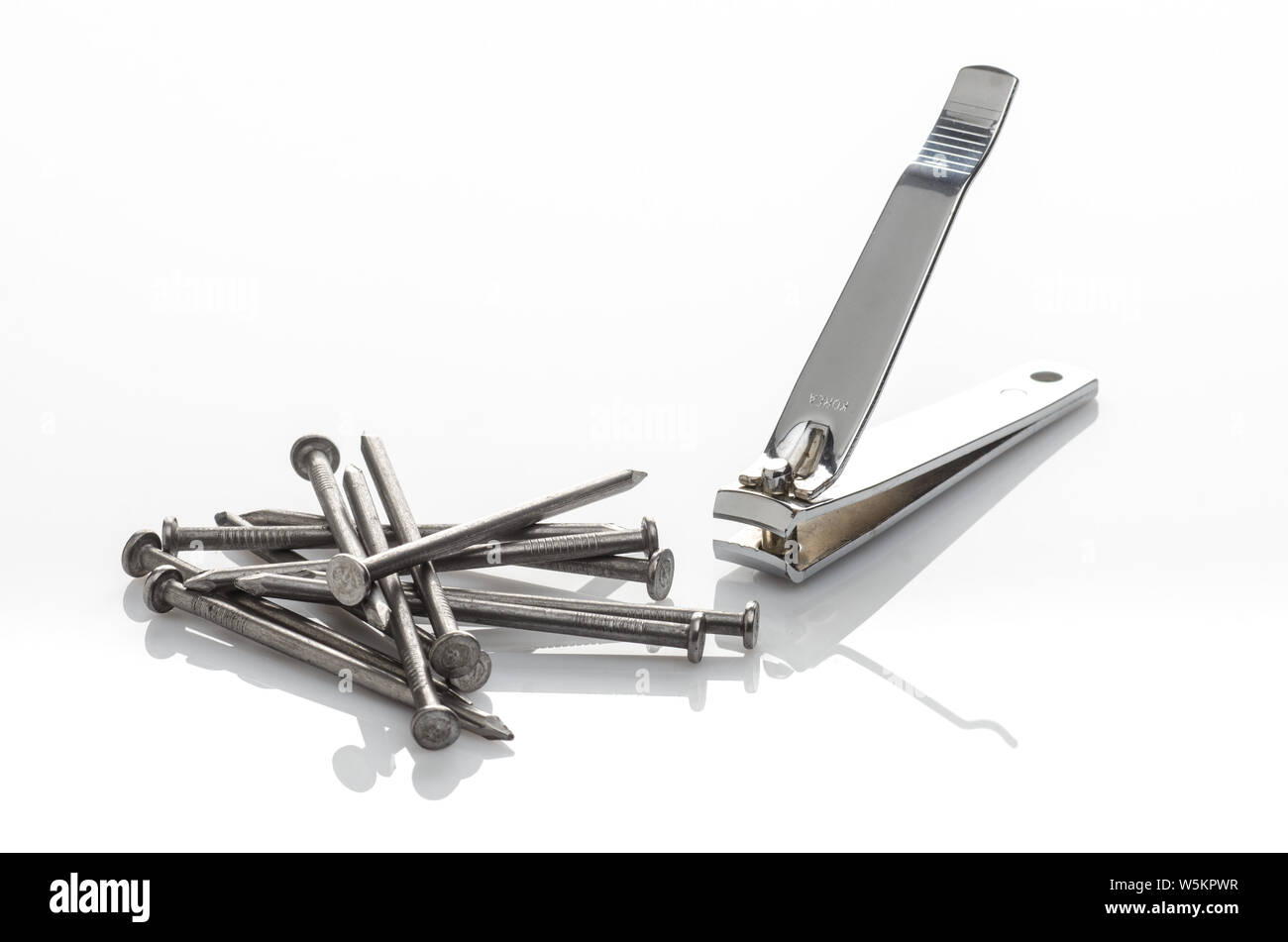 Studio still-life photo of nail clippers and several nails (hardware) on a reflective white background. Stock Photo