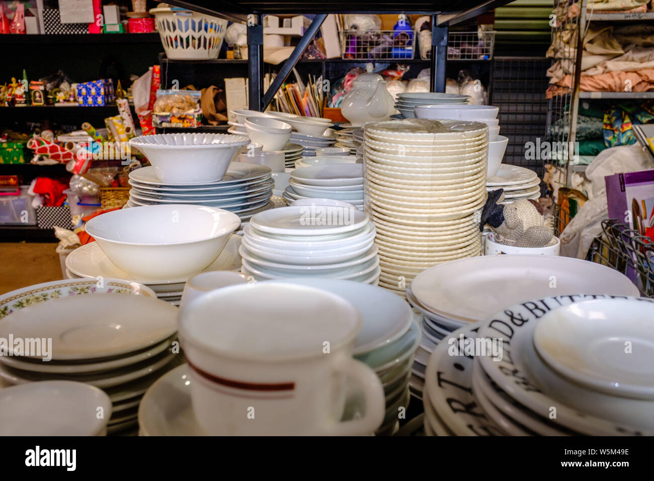 Piles of plates, crockery and ceramics on shelves in charity shop interior view, charity chic for up cycle, recycle, reuse and re purpose. Stock Photo