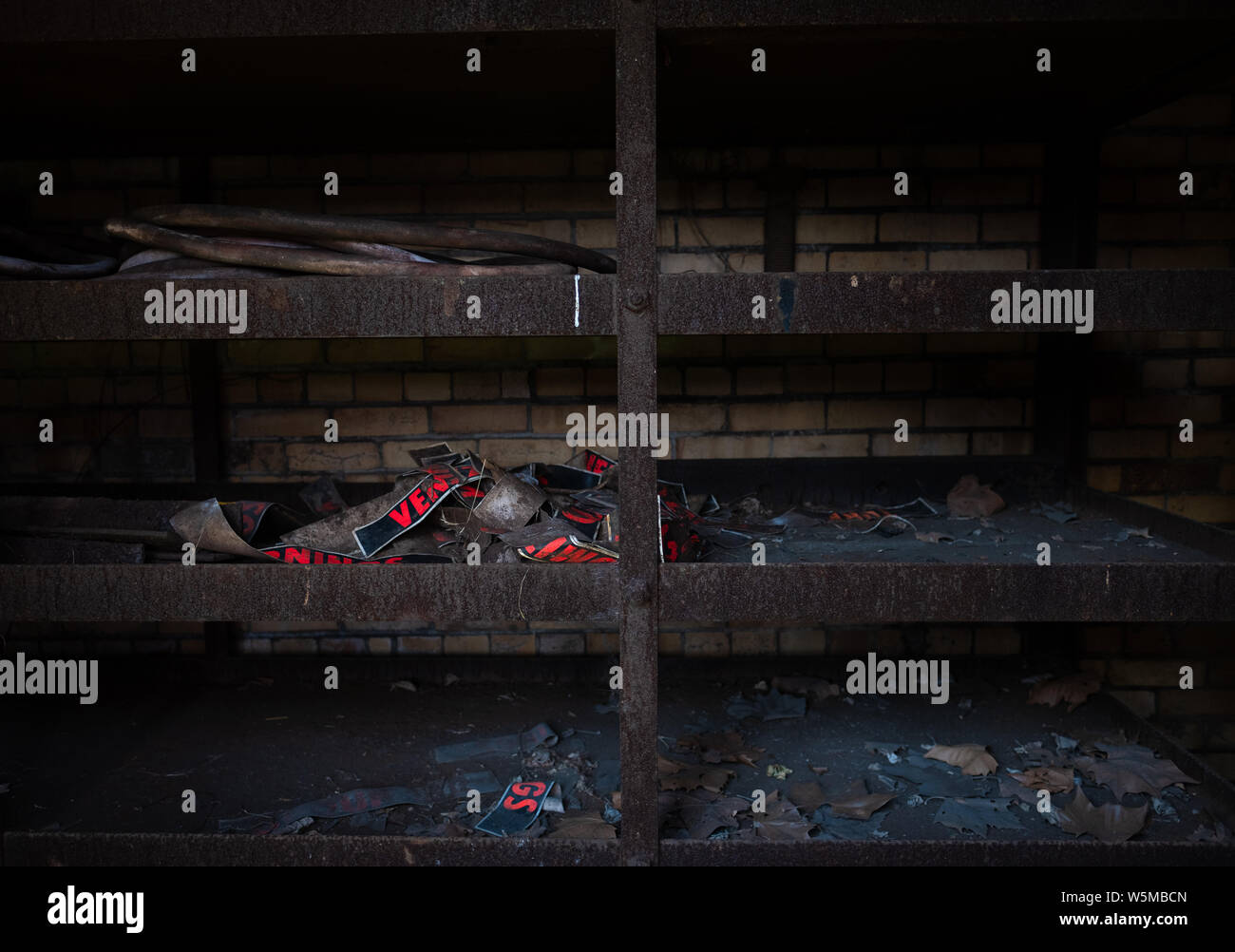 Old rusty metal shelving unit with remnants of discarded signs inside a dark abandoned industrial space Stock Photo