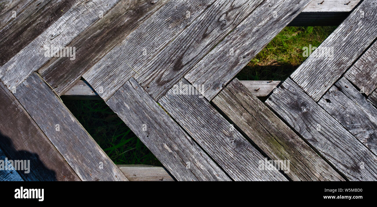 Weathered, graying wooden planks arranged in a herringbone pattern, with some planks missing Stock Photo