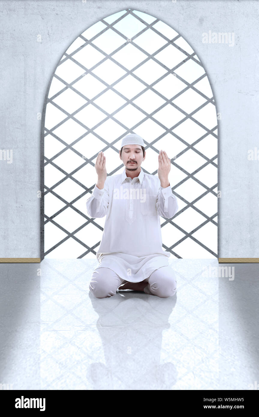 Asian Muslim man sitting in pray position while raised hands and