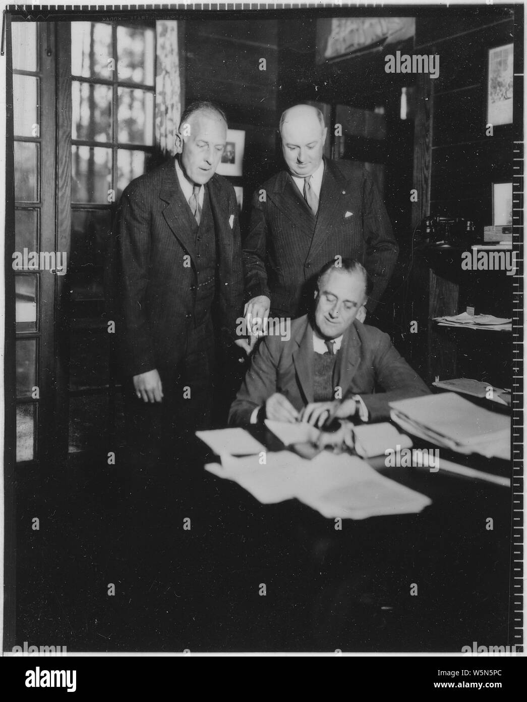 Franklin D. Roosevelt, Farley, and Charles Richard Crane in Warm Springs, Georgia; General notes:  Charles R. Crane (left) and James Farley stand behind FDR who is signing a document. Stock Photo