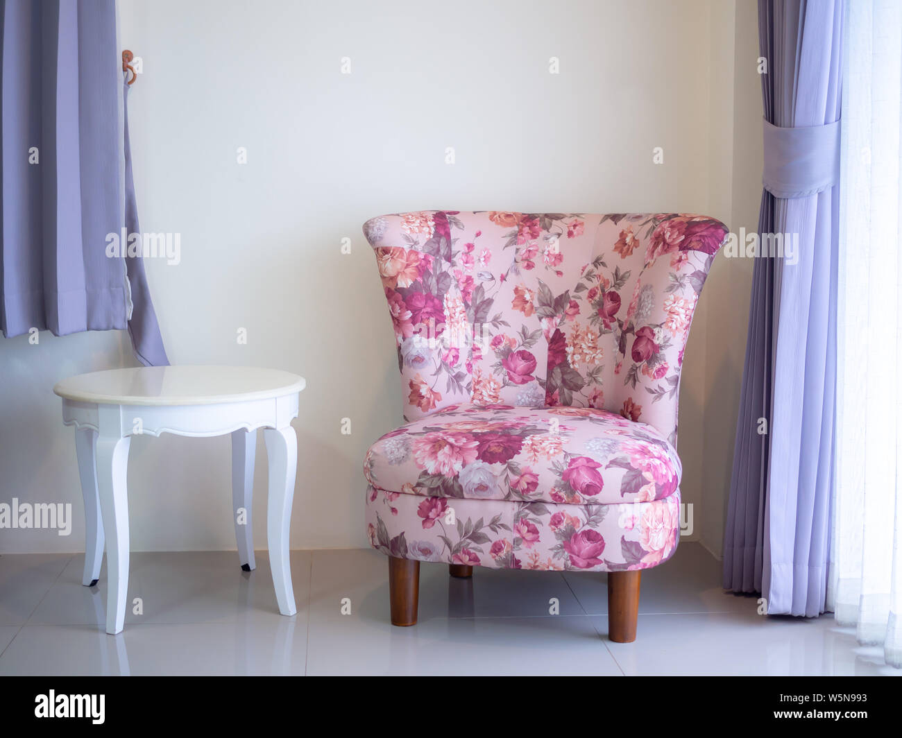 Beautiful pink vintage sofa and white round desk on white wall background near the window. Stock Photo