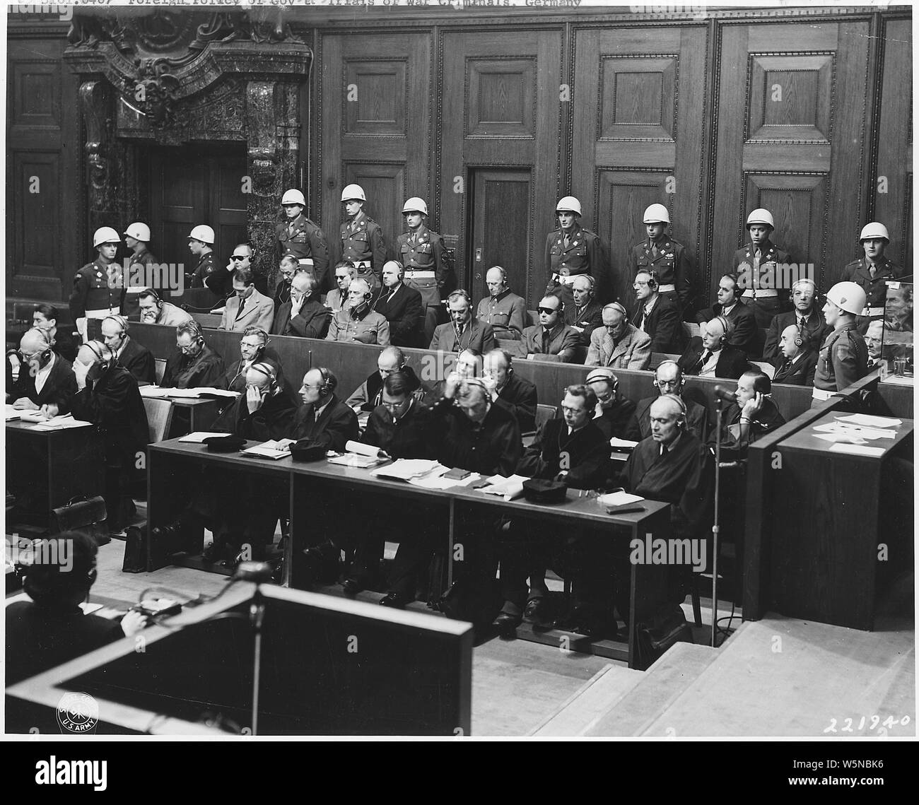 German War Crimes Trials. Nuernberg & Dachau; Scope and content:  The prosecution charges the defendants with conspiring to destroy the independence of other nations. Goering is in the defendant's box. The defendants, surrounded by American military police, Goering, Hess, Von Ribbentrop, Keiter, Rosenberg, Frank, Frick, Streicher, Funk, Schacht; back row, Donitz, Raeder, Von Schirach, Sauckel, Jodl, Von Papen, Seyss-Inquart, Speer, Von Neurath, and Hans Fritsche. 11/23/45. Stock Photo