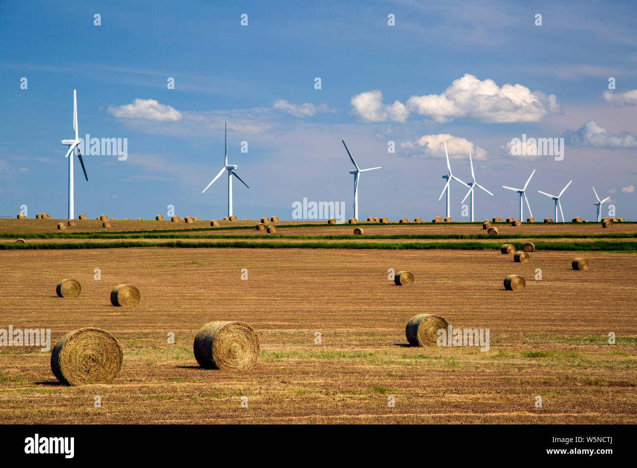 Renewable energy wind turbines in a harvested agricultural field with bales hay in the Canadian prairies of Alberta, Canada. Stock Photo