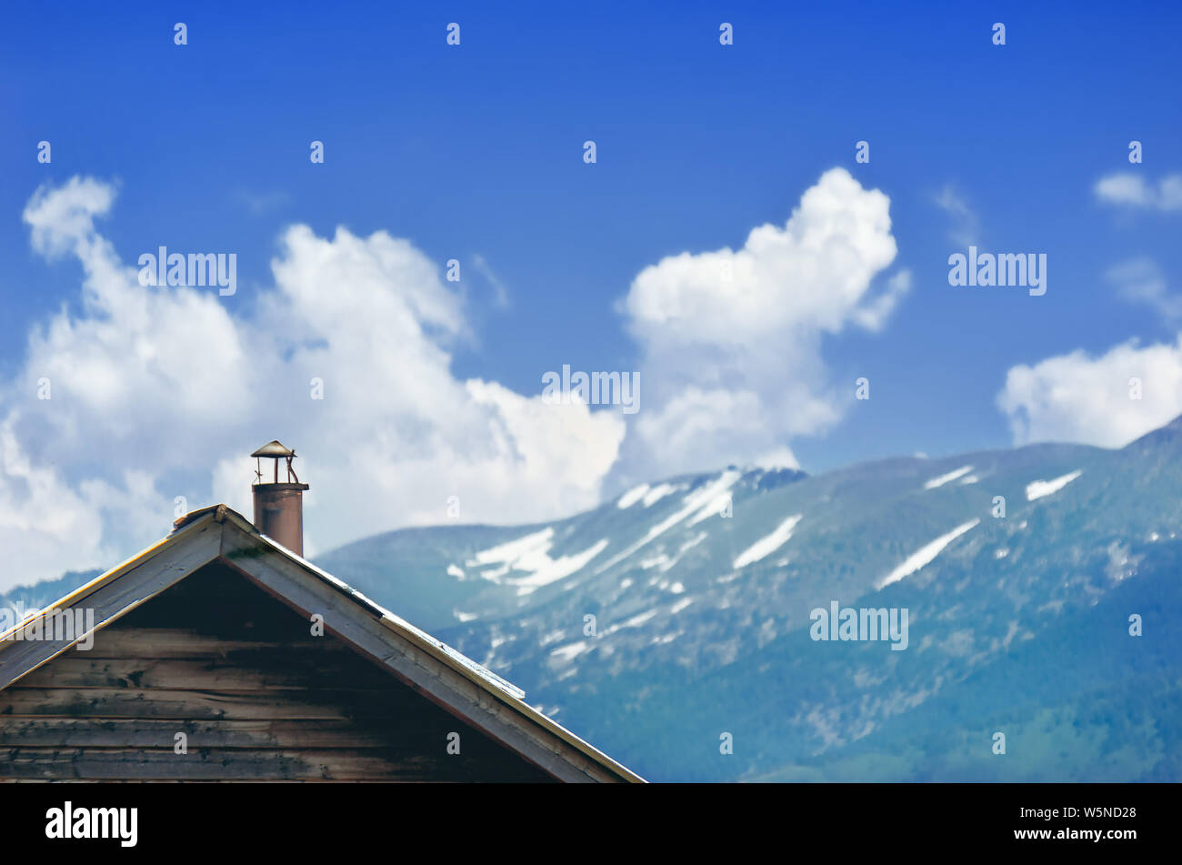 Gable End of an Aged Cottage with Horizontal Wooden Siding, Metal Chimney. Altai Mountains with White Snow Caps, Kazakhstan. Stock Photo