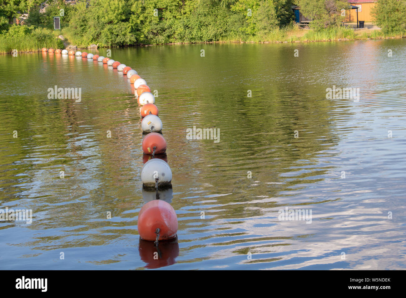 A barrier of floating buoys blocks a river, preventing boats from heading towards an open dam. Stock Photo