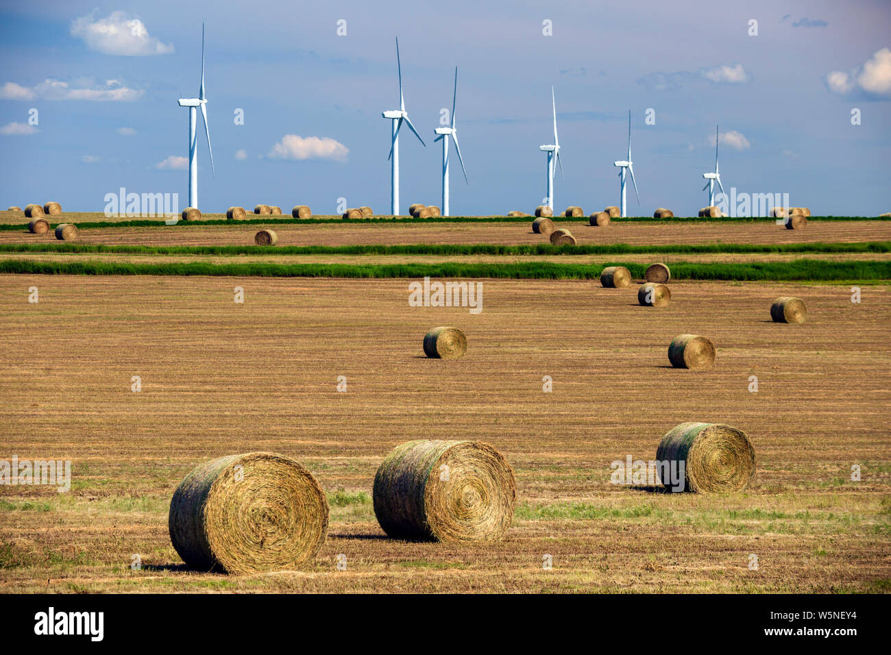 Renewable energy wind turbines in a harvested agricultural field with bales hay in the Canadian prairies of Alberta, Canada. Stock Photo