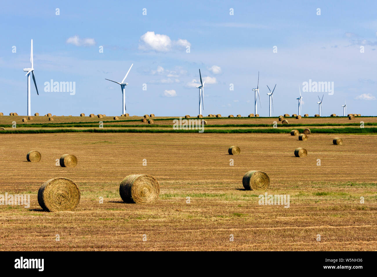 Renewable energy wind turbines in a harvested agricultural field with bales hay in the Canadian prairies of Alberta, Canada. Stock Photo