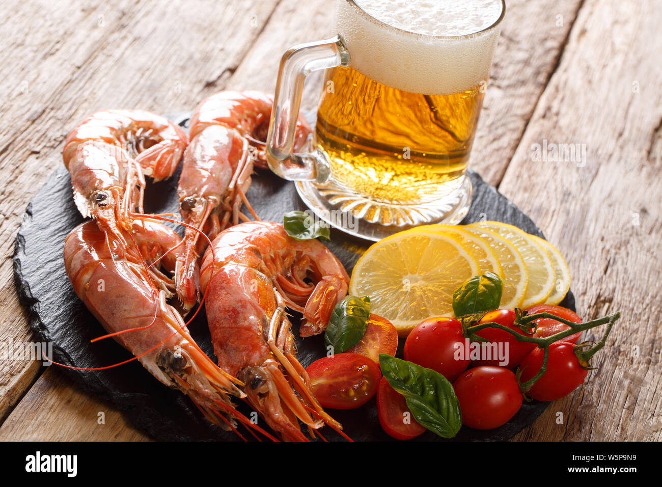 Traditional light beer and tasty shrimps, lemon and tomatoes close-up on a slate board on the table. horizontal Stock Photo