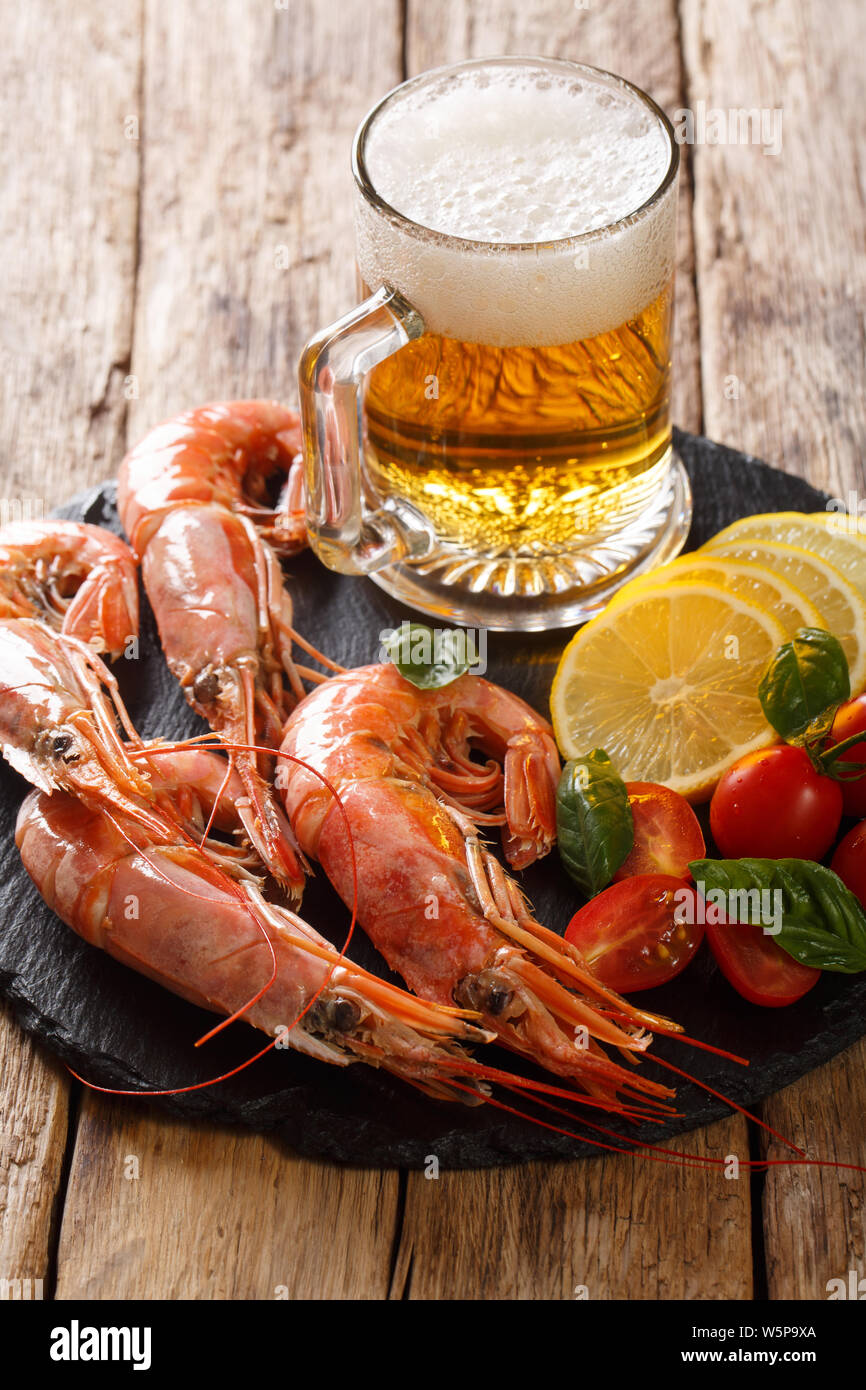 glass of beer and delicious shrimps, lemon and tomatoes close-up on a slate board on the table. Vertical Stock Photo