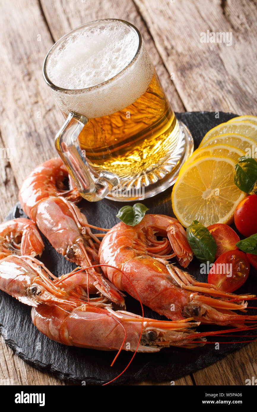 foamy beer with tasty shrimps, lemon and tomatoes close-up on a slate board on the table. Vertical Stock Photo