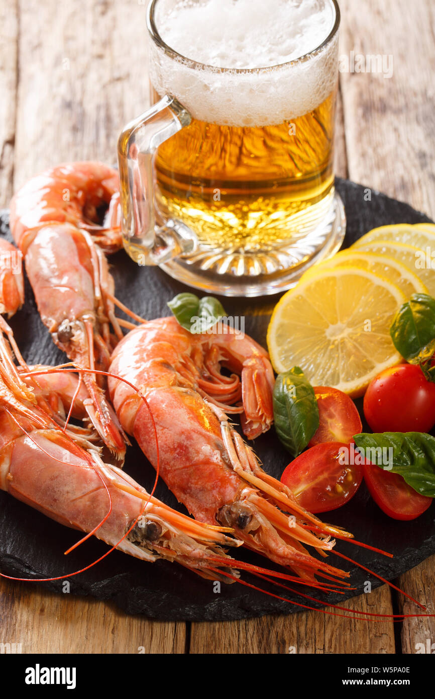 Snack to beer delicious shrimp, lemon and tomatoes close-up on a slate board on the table. Vertical Stock Photo
