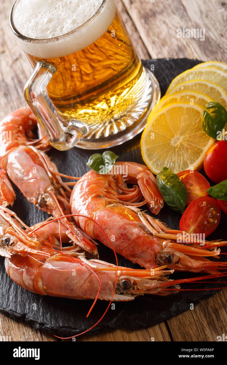 Spicy king prawns with light beer, lemon and tomatoes close-up on a slate board on the table. Vertical Stock Photo