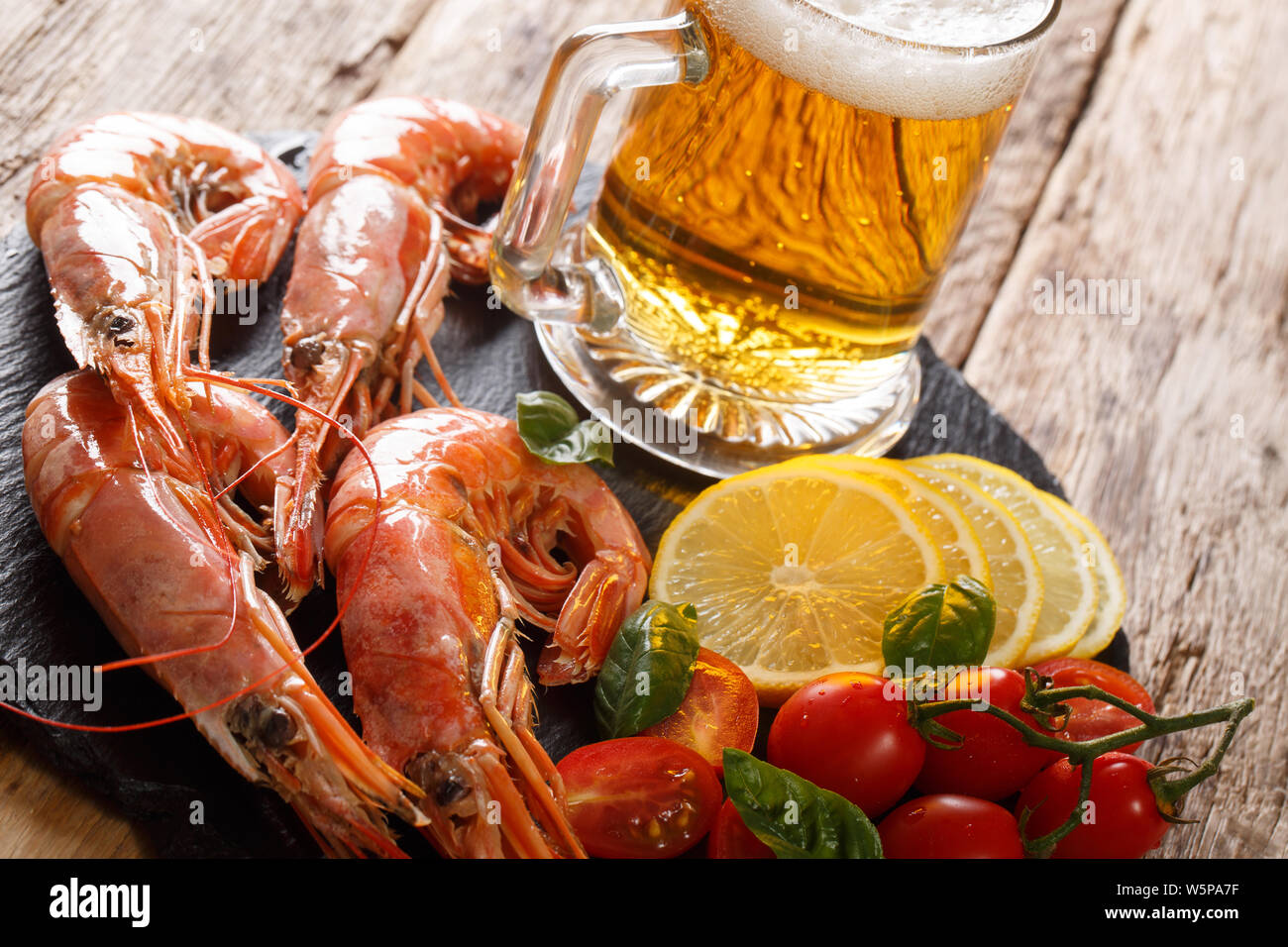 Delicious king prawns with light beer, lemon and tomatoes close-up on a slate board on the table. horizontal Stock Photo