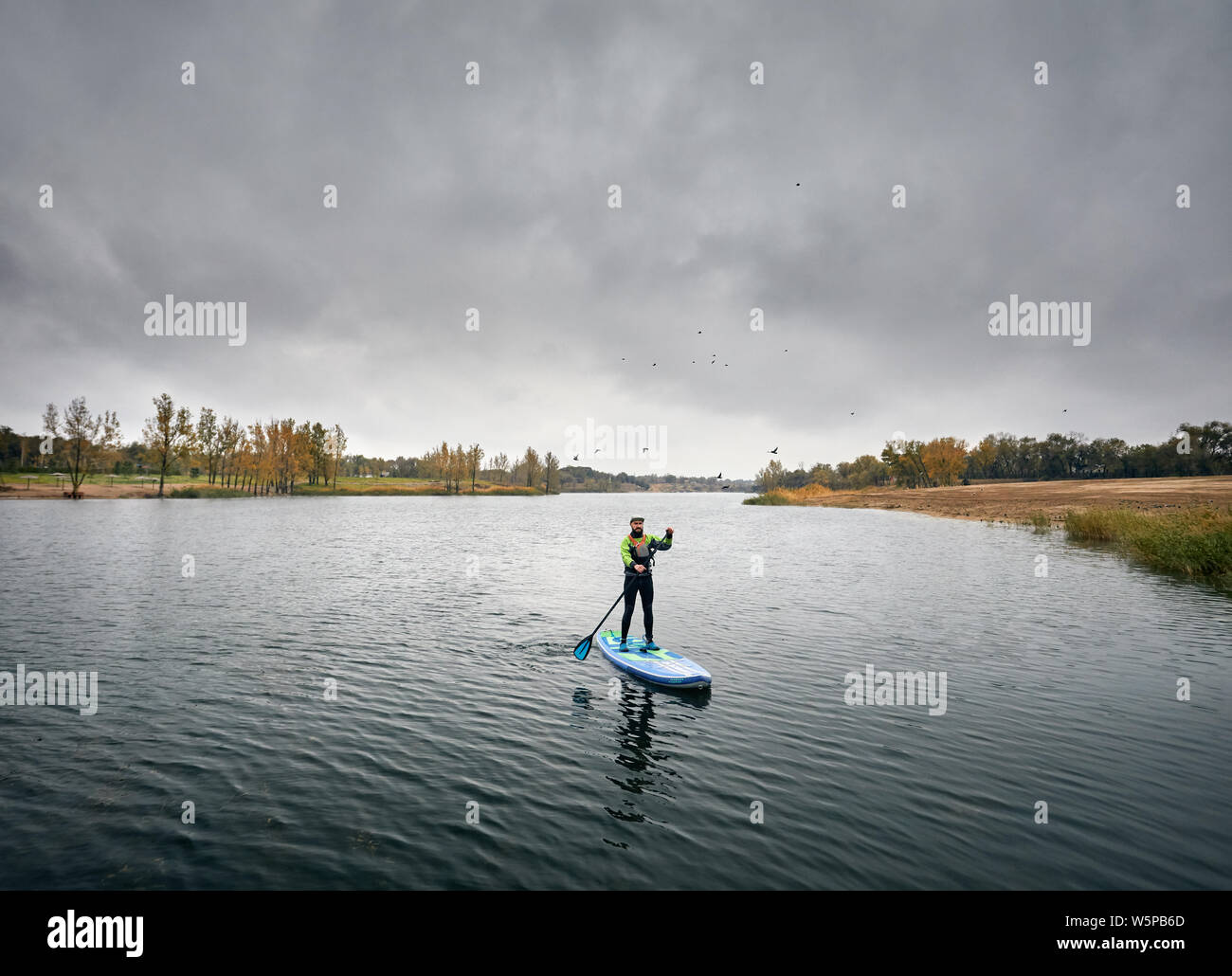 Man training on paddleboard in the lake against overcast sky Stock Photo